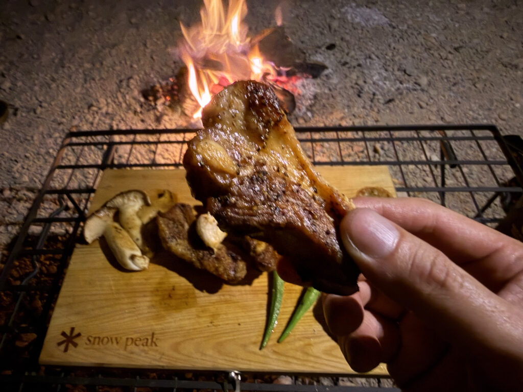 直火とスキレットで焼き上げた豚スペアリブを手に持って食べている様子