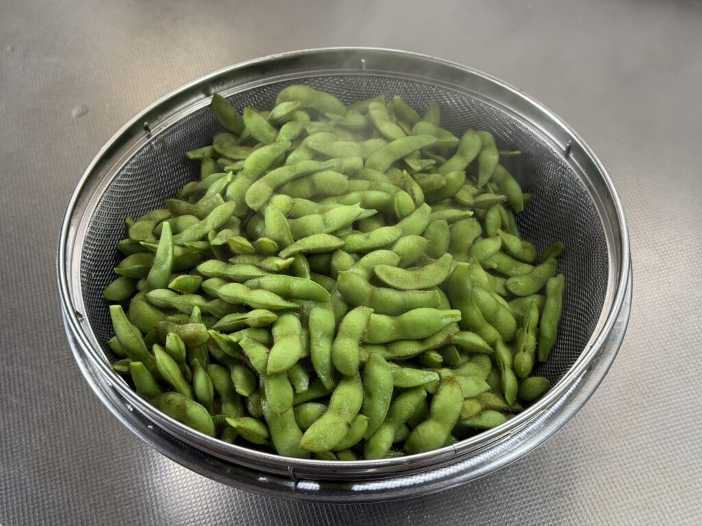 塩茹でしてザルへ上げた湯気の立つ枝豆