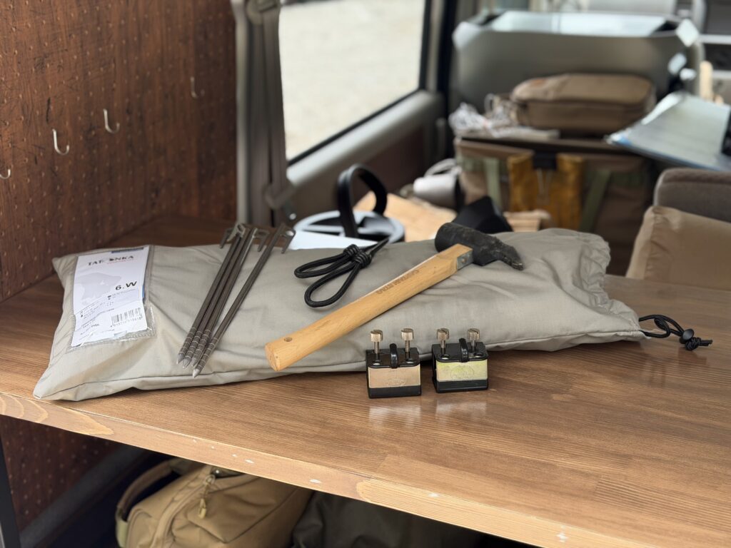 エブリイ車内のテーブルに置いたTatonka Tarp 4 TC、チタンペグ、ハンマー、ガイロープ、カージョイント