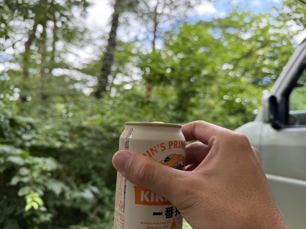木々に囲まれた13番サイトで設営途中に缶ビールを持って乾杯する様子
