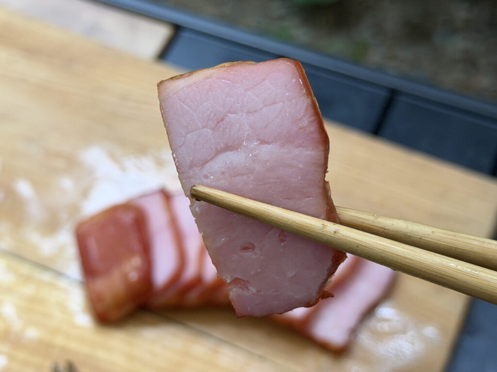 厚く切り分けて箸で持ち上げたブロックベーコンの燻製