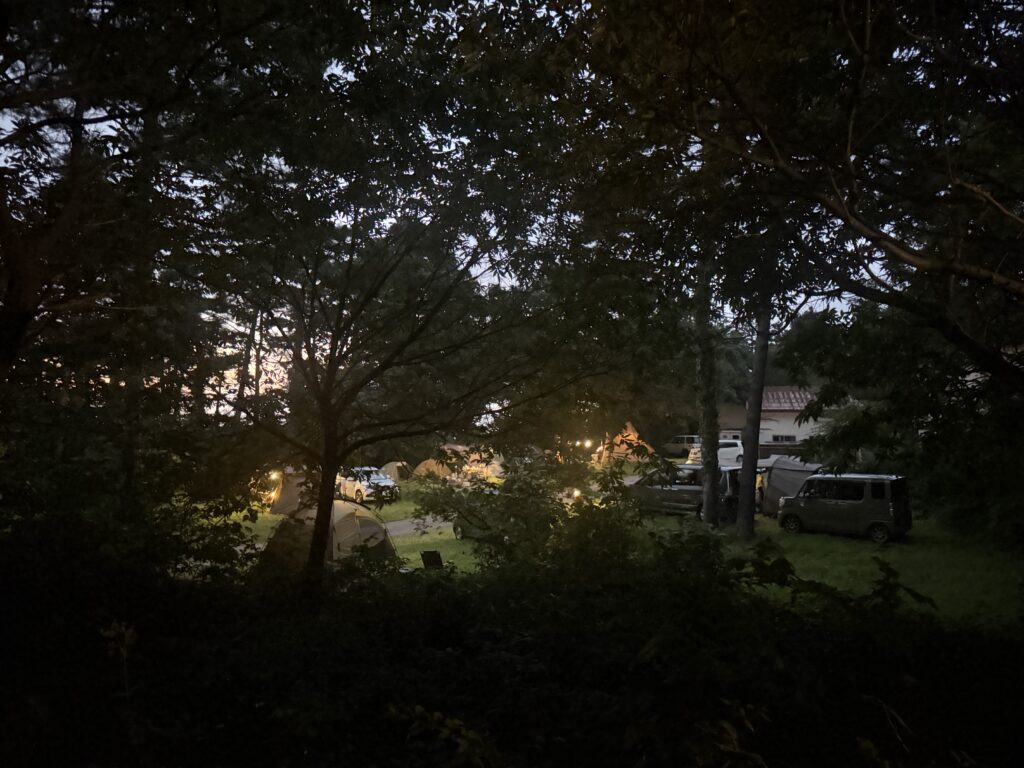 夕暮れの木々の間から見えるキャンパーのテントとランタンの明かり