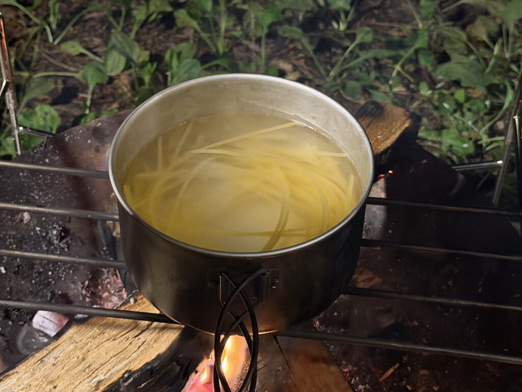 焚き火の上に載せたクッカーでパスタを茹でる様子