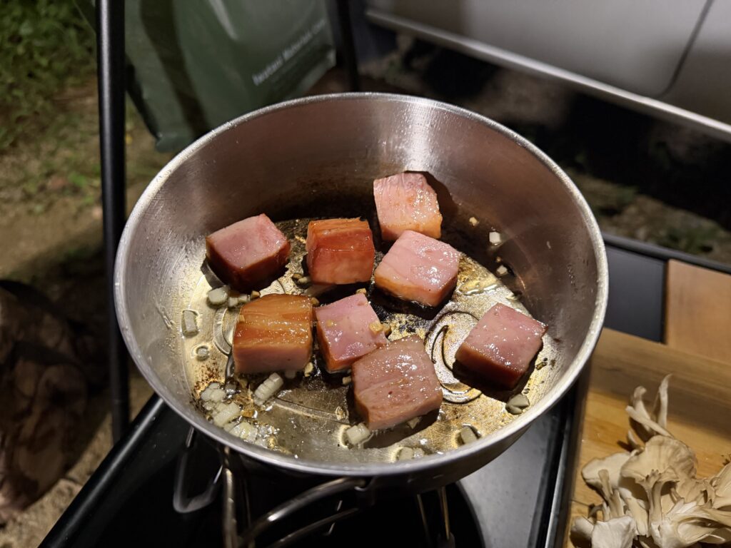 SOTO ST-310に載せたフライパンでにんにくと燻製ベーコンを加熱する様子