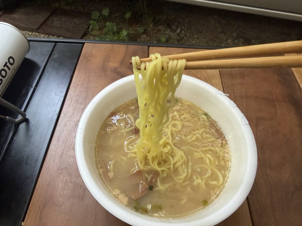 キャンプ場の朝食に天下一品のカップ麺を箸で持ち上げて食べる様子