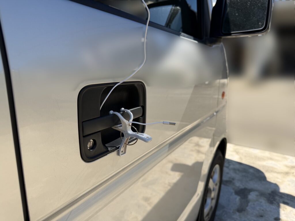 エブリイの運転席側ドアハンドルにクリップを取り付け、日陰で車外温度センサーを固定した様子