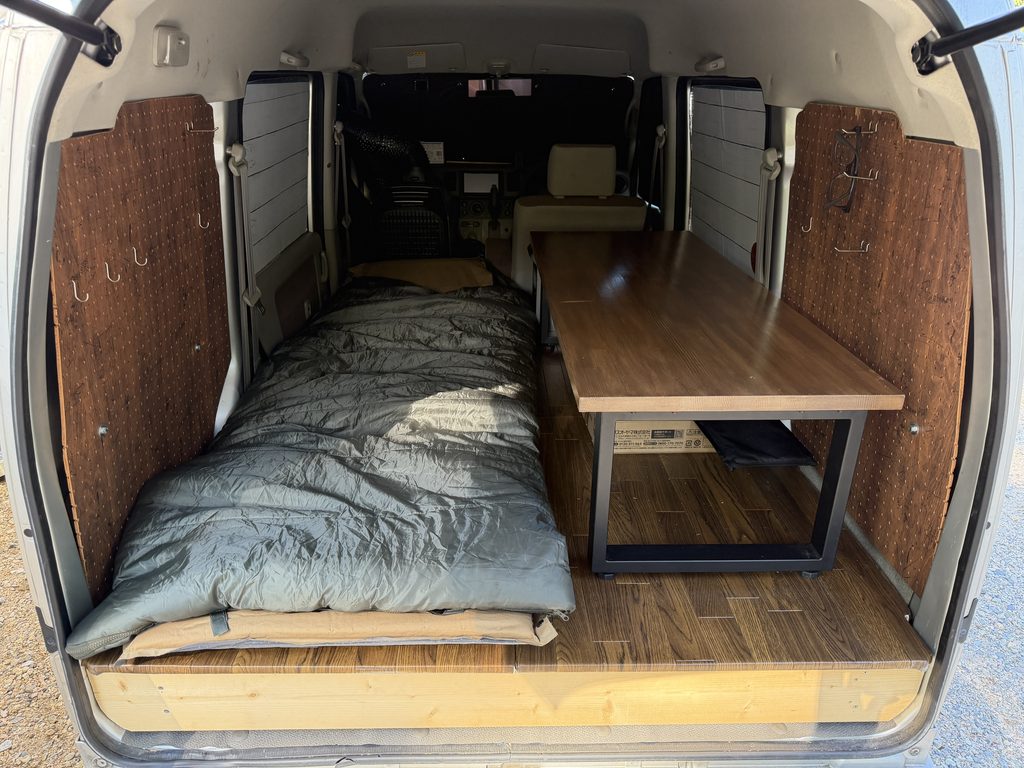 左側に寝具、右側に木製テーブルを配置したエブリイの車中泊仕様の荷室