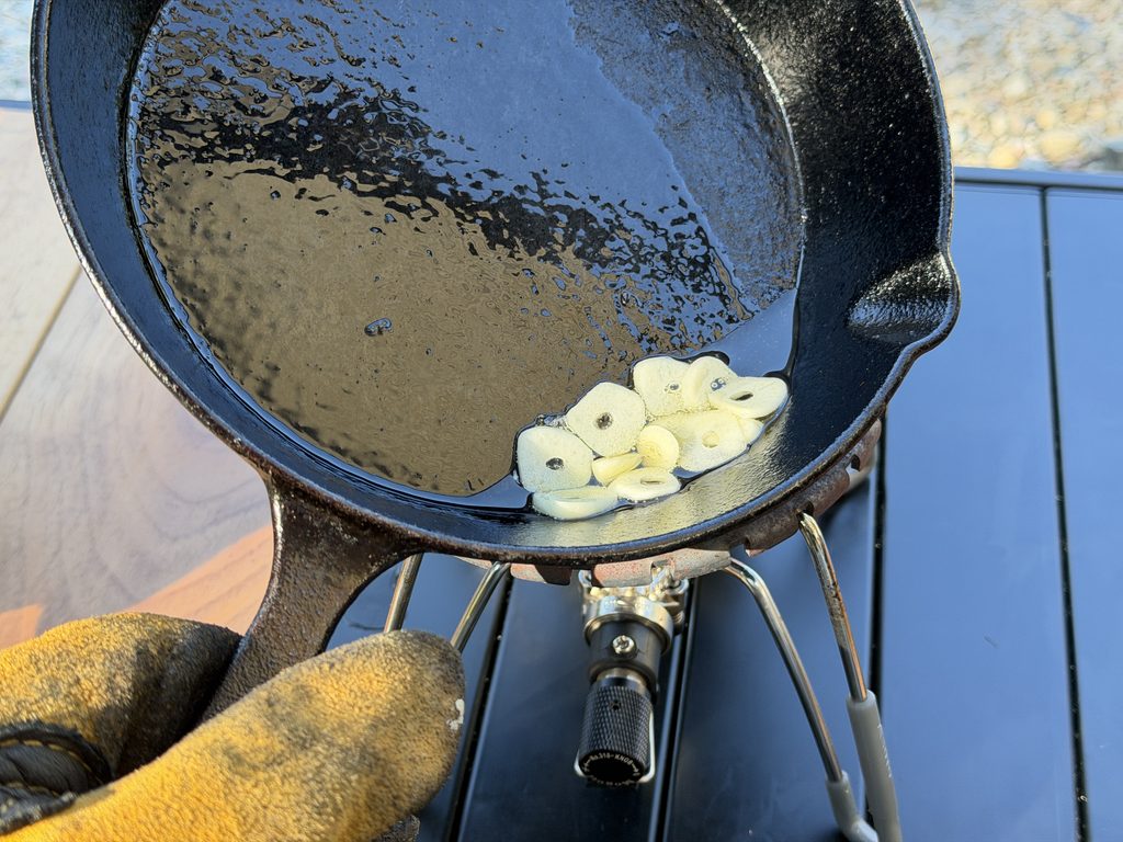 スキレットのオリーブオイルでスライスしたニンニクを加熱する様子