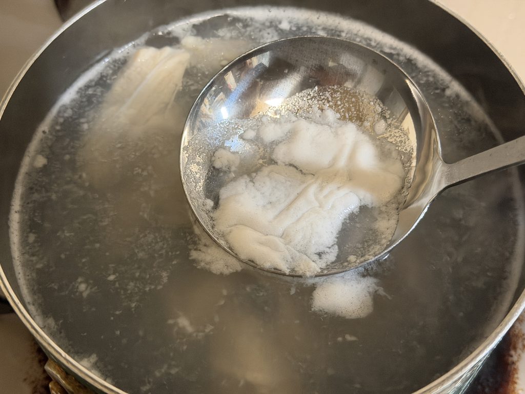 ヤゲン軟骨を茹でながら、お玉で浮いてきたアクを取り除いている様子